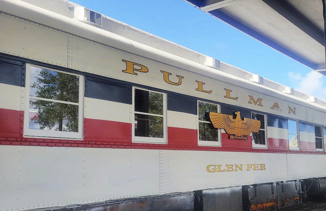A restored Pullman railcar named Glen Fee sits on the tracks at the Galveston Railroad Museum, painted in red, white, and black with gold lettering and an eagle emblem on the side.