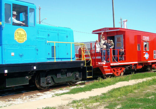 Blue locomotive pulling red caboose with passengers Blue locomotive pulling red caboose with passengers