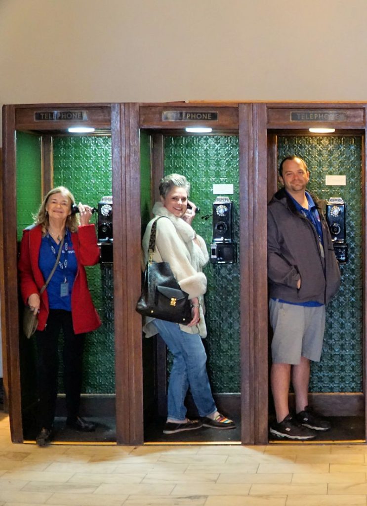 Three people posing in vintage phone booths