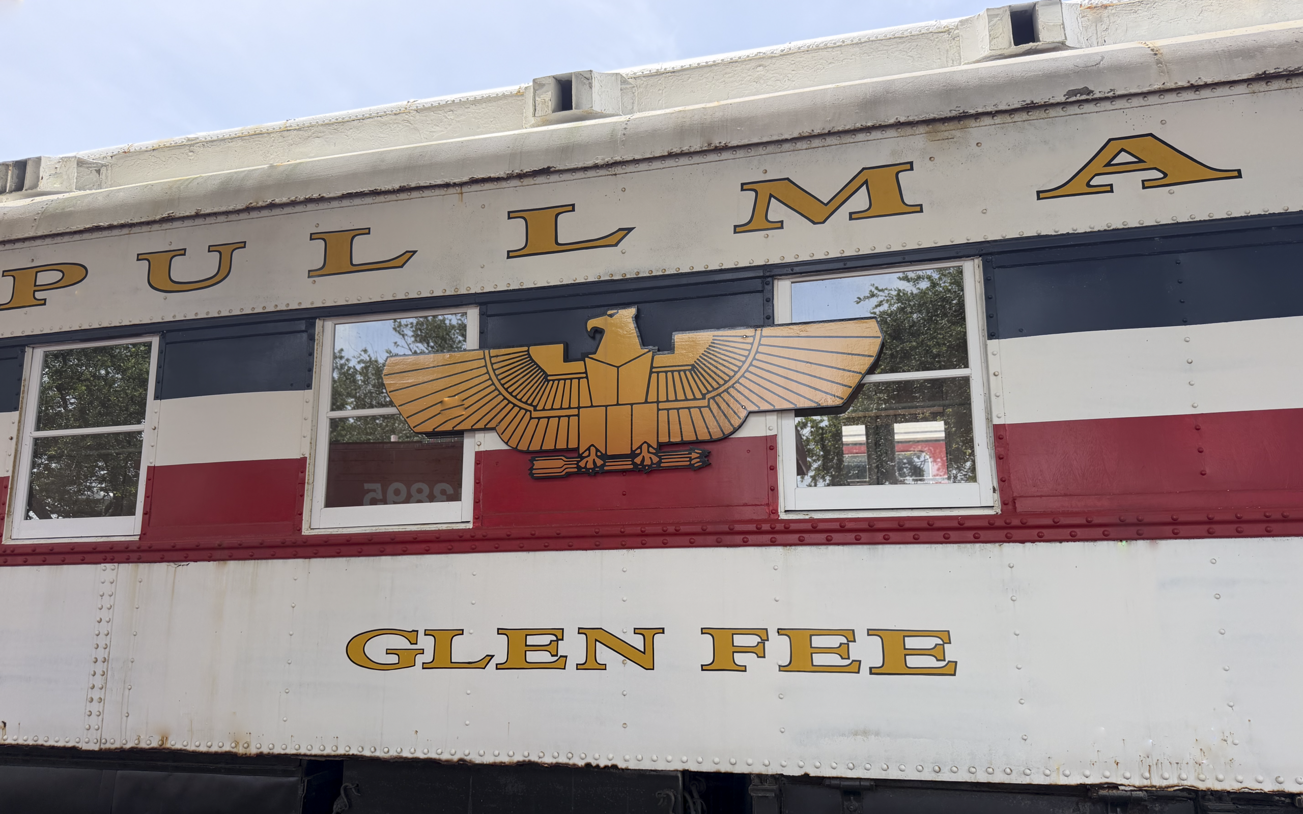 Side view of the Glen Fee Pullman railcar at the Galveston Railroad Museum, painted in red, white, and blue stripes with gold lettering and a gold spread-eagle emblem on the exterior.