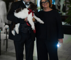 Two people posing with fluffy dog indoors
