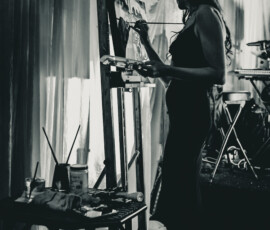 Artist painting at easel beside draped curtains